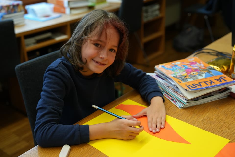 Kind malt mit Buntstift auf buntem Papier.