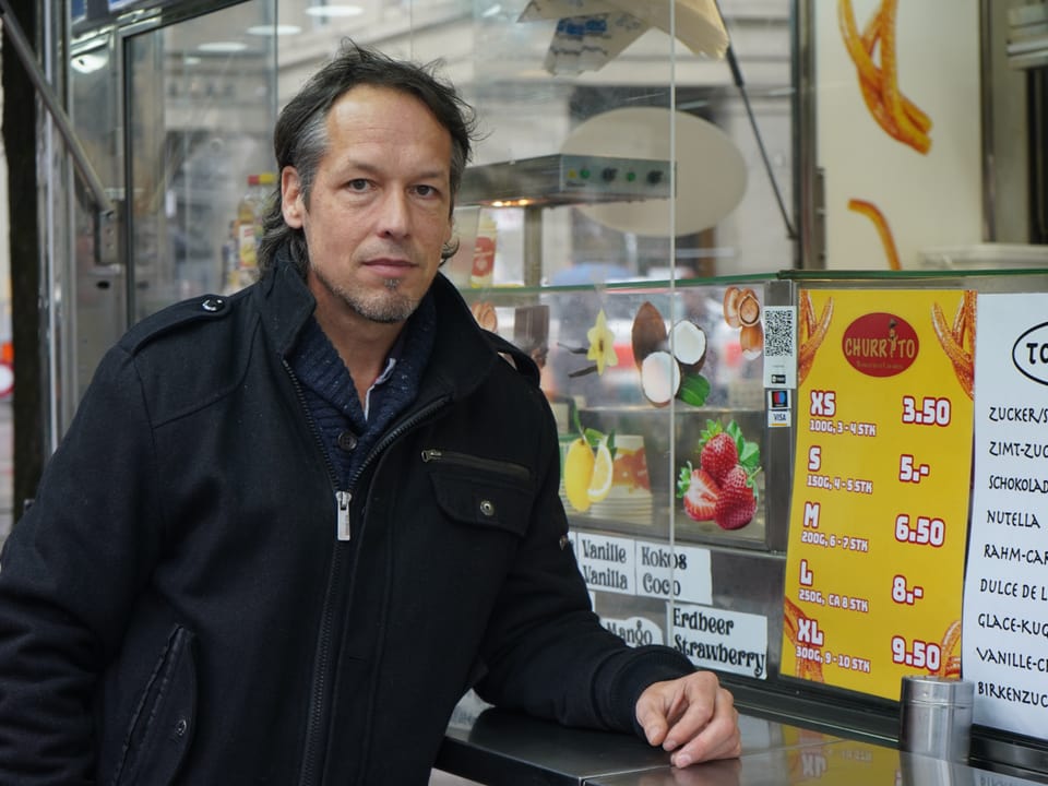 Mann in schwarzer Jacke vor einem Churro-Stand.