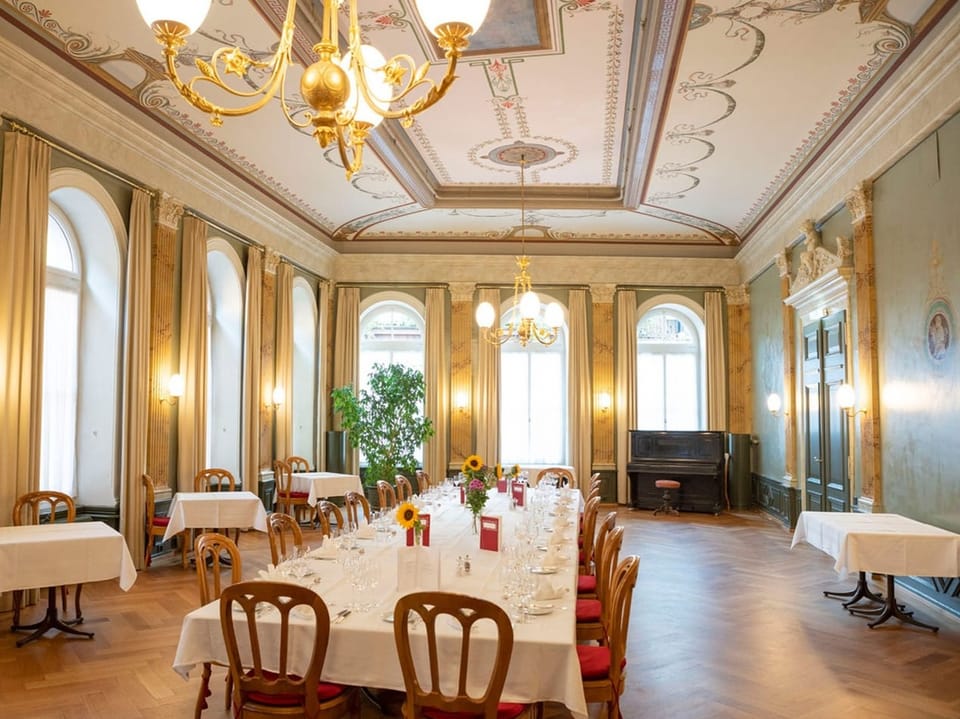 Speisesaal mit grossem Tisch in der Mitte und Leuchter an der Decke.