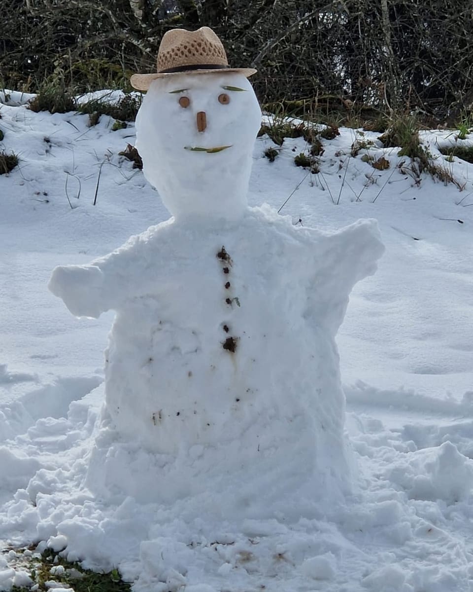 Schneemann mit Strohhut im Schnee.