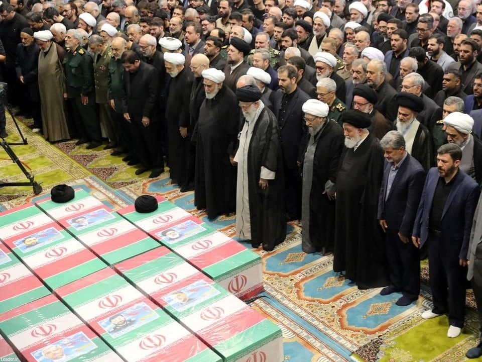Menschen, die neben Särgen mit der iranischen Flagge stehen.