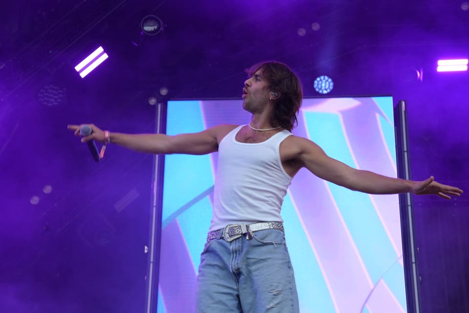 Mann in weissem Tanktop singt auf der Bühne mit ausgestreckten Armen am Open Air Lumnezia 2024.