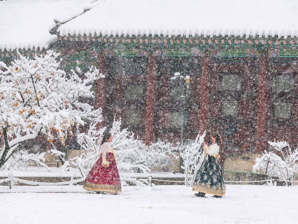 zwei frauen laufen in traditionellen Röcken über einen schneebedeckten Platz.