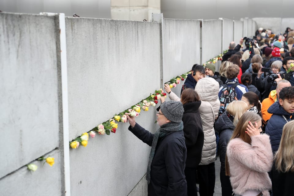 Menschen legen Blumen an eine Betonmauer.