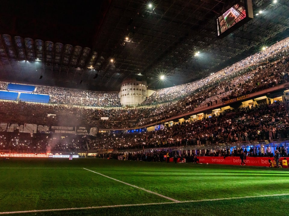 Gefülltes Fussballstadion bei Nacht mit beleuchteten Rängen.