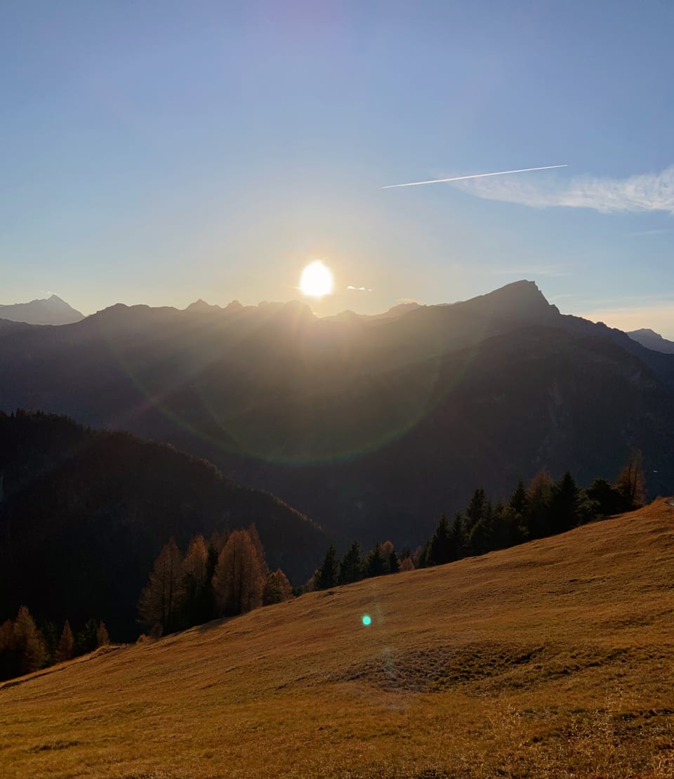 Sonnenuntergang über Berglandschaft mit Wolken und Wiese.