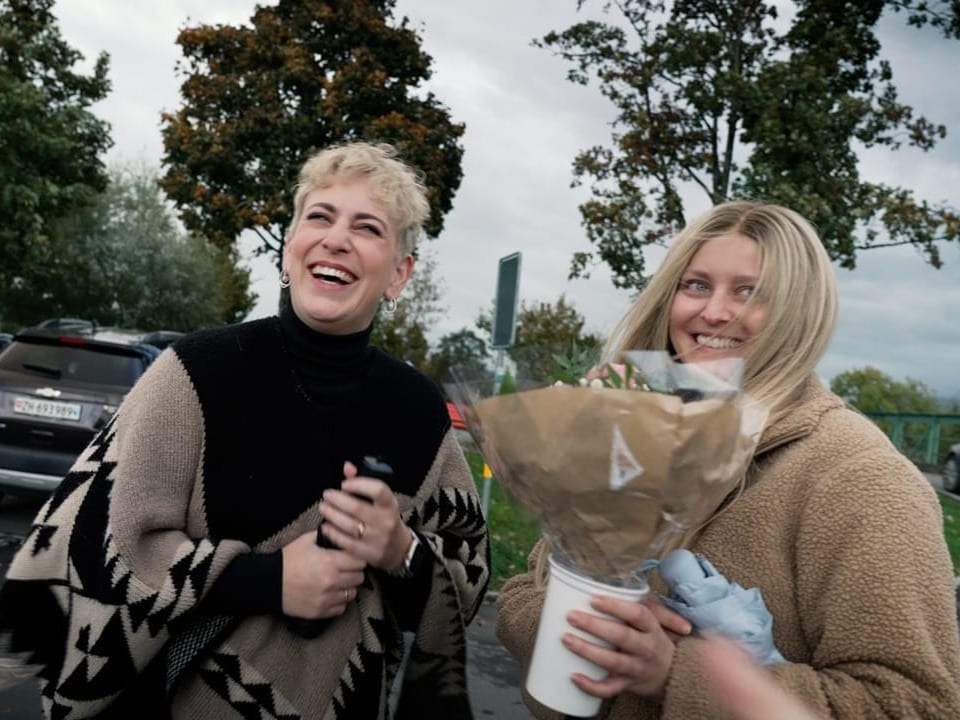 Stefanie und Caroline beim ersten Treffen auf Parkplatz, Caroline hat Blumenstrauss in der Hand