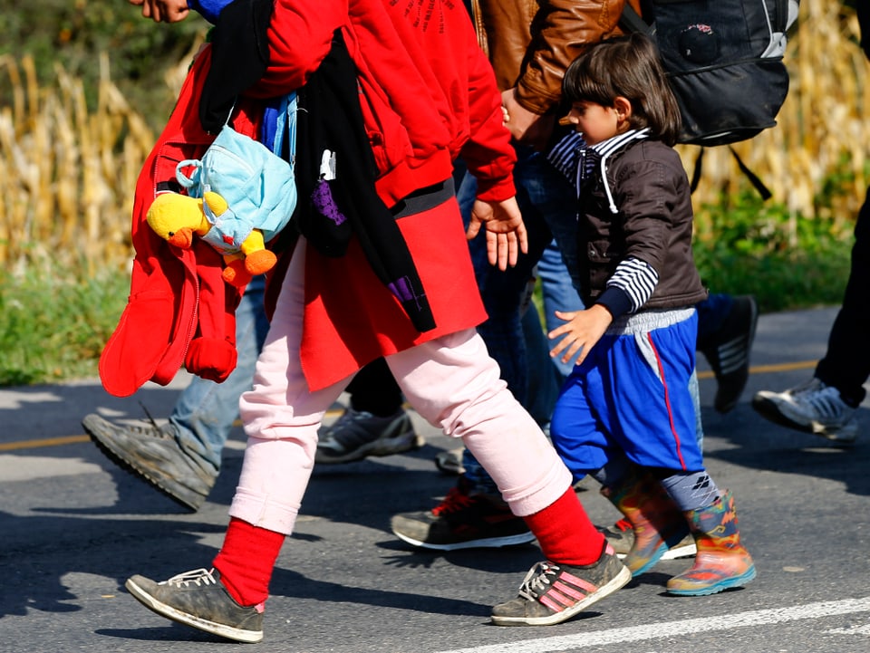 Eine Flüchtlingsfamilie mit Kindern zu Fuss auf einer Strasse