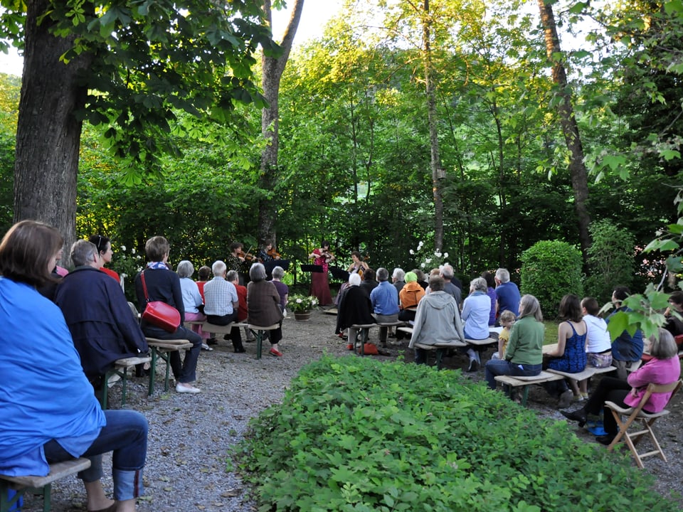 Publikum sitzt im Garten und lauscht einer Geigenspielerin.