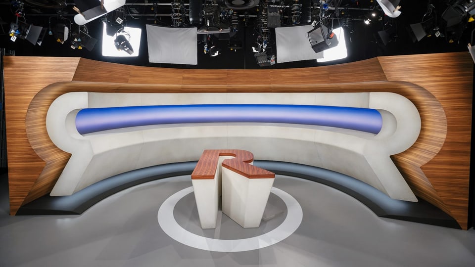 Moderner TV-Studiotisch mit Holzelementen und blauer Lichtleiste.