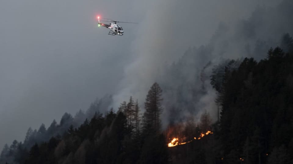 Ein Helikopter fliegt ob einem Waldbrand.