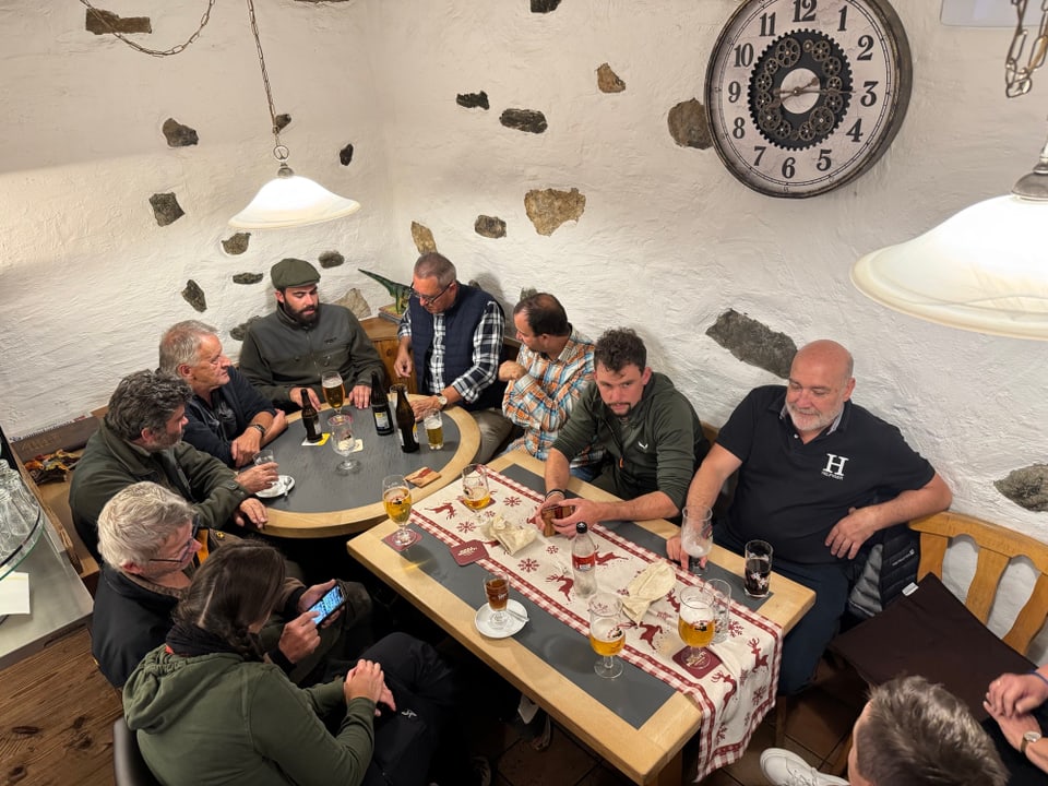 Gruppe von Menschen sitzt um einen Tisch in einer rustikalen Kneipe.