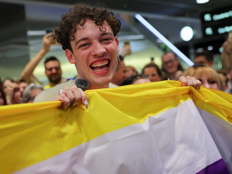 Junger Person hält eine gelb-weisse Fahne und lacht glücklich in einer Menschenmenge.