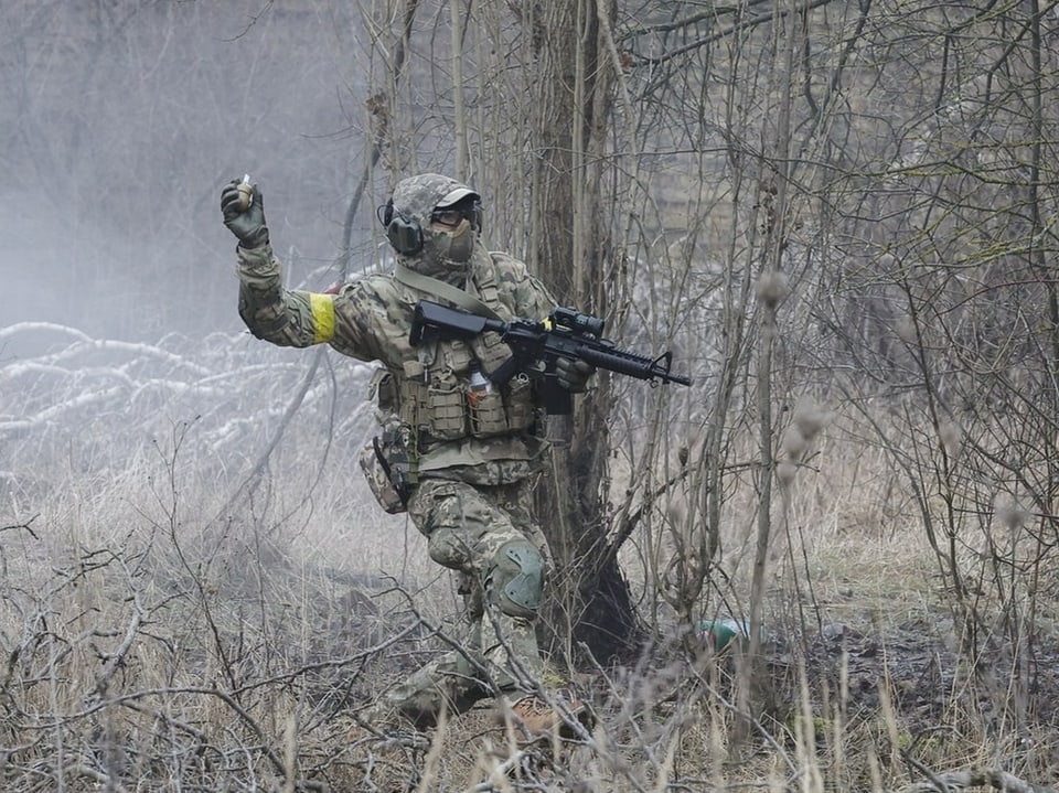 Ein ukrainischer Zivilist rennt in Vollmontur auf einer Wiese und wirft eine Granaten-Attrappe.