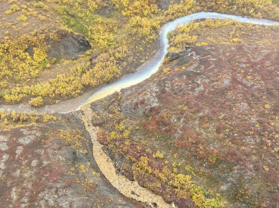 Ein Fluss und ein Bach mit orange-Färbung fliessen durch eine Landschaft.