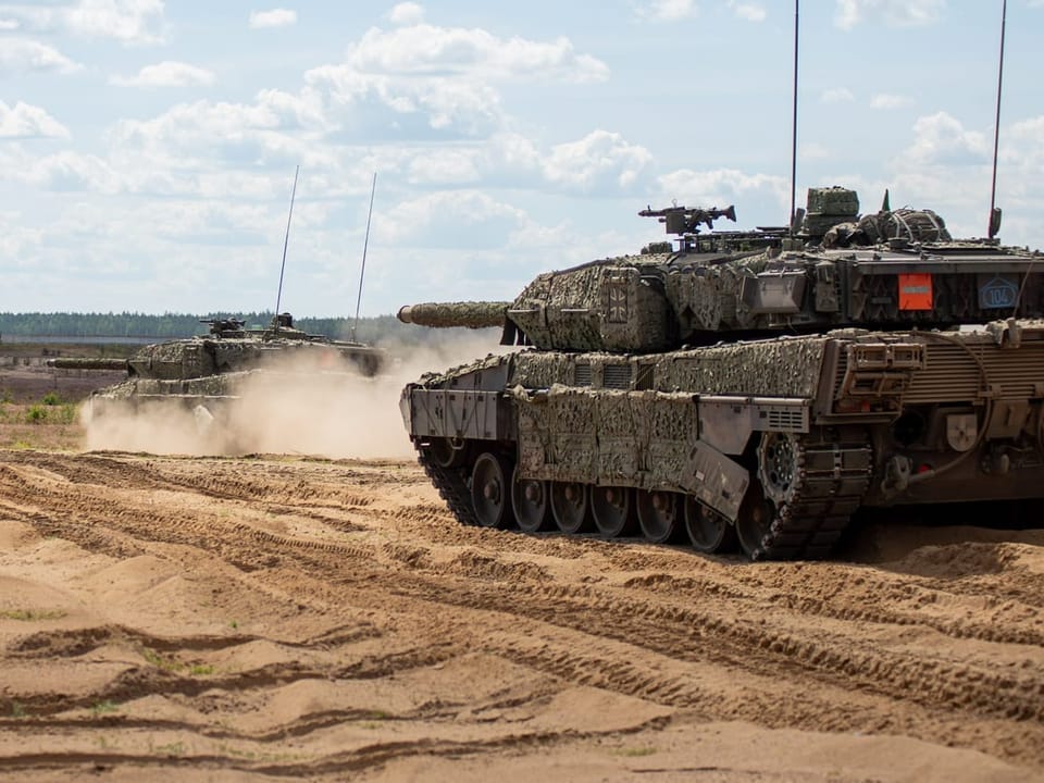 Zwei Panzer fahren durch eine sandige Landschaft.