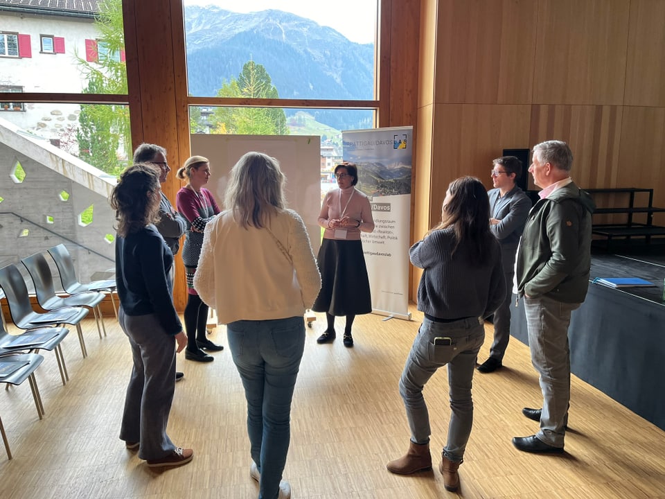 Personengruppe steht im Kreis in Holzzimmer mit Bergblick.