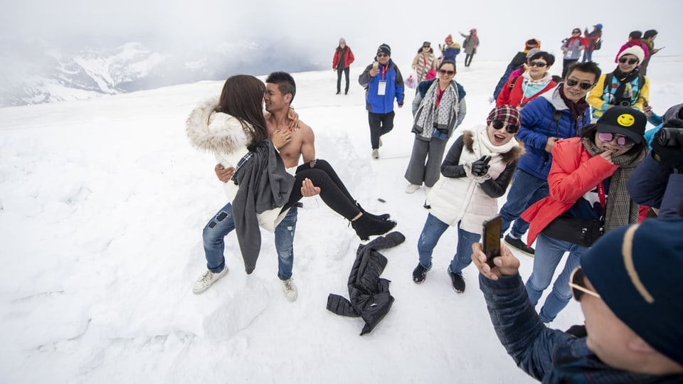 Touristinnen und Touristen aus China freuen sich im Schnee.