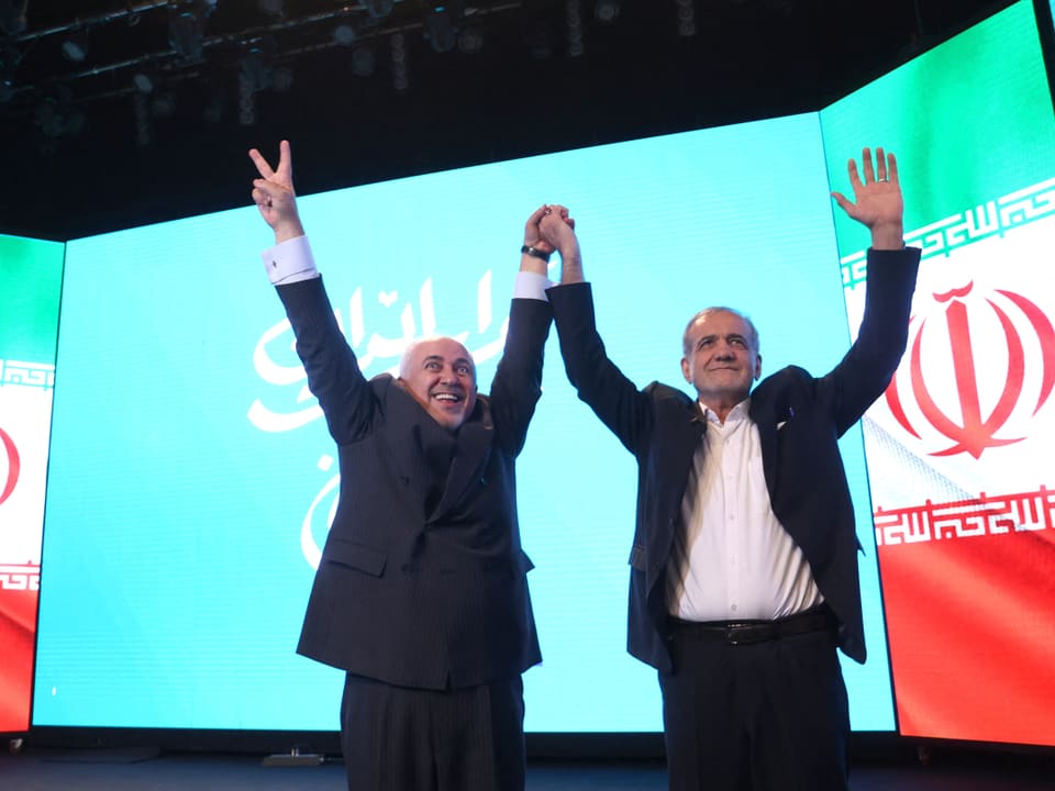 Zwei Männer halten ihre Hände vor einer Leinwand mit der iranischen Flagge.