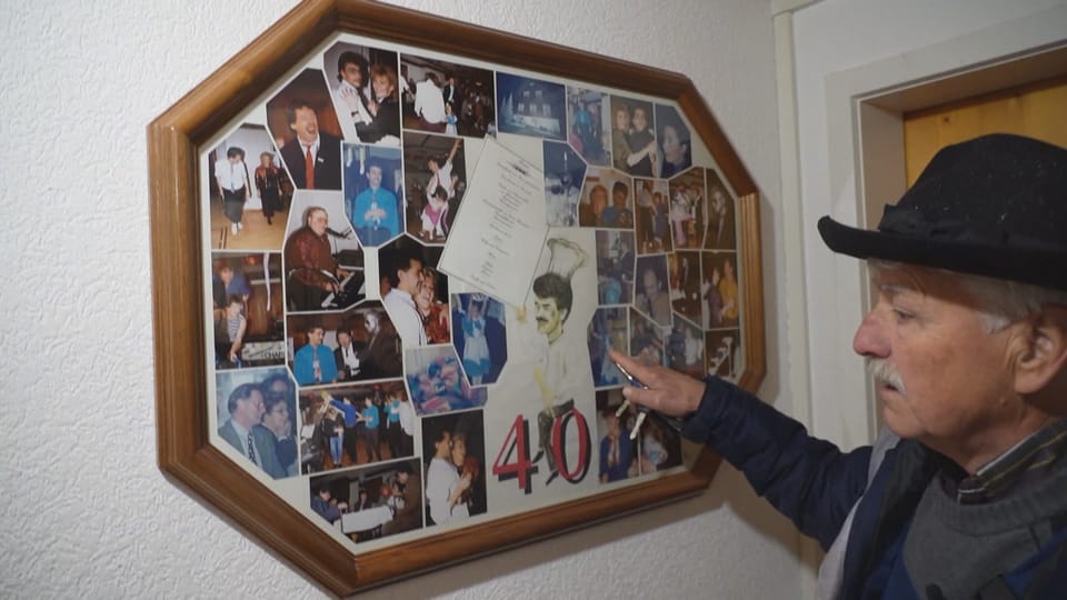 Rechts älterer Mann mit Hut, links eine Fotocollage an der Wand, auf der «40» steht.