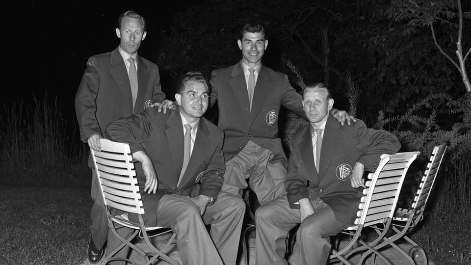 Vier Herren im Anzug posieren in einem Garten.
