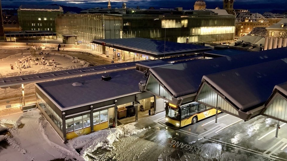 Verschneiter Busbahnhof mit beleuchtetem Gebäude in der Abenddämmerung.