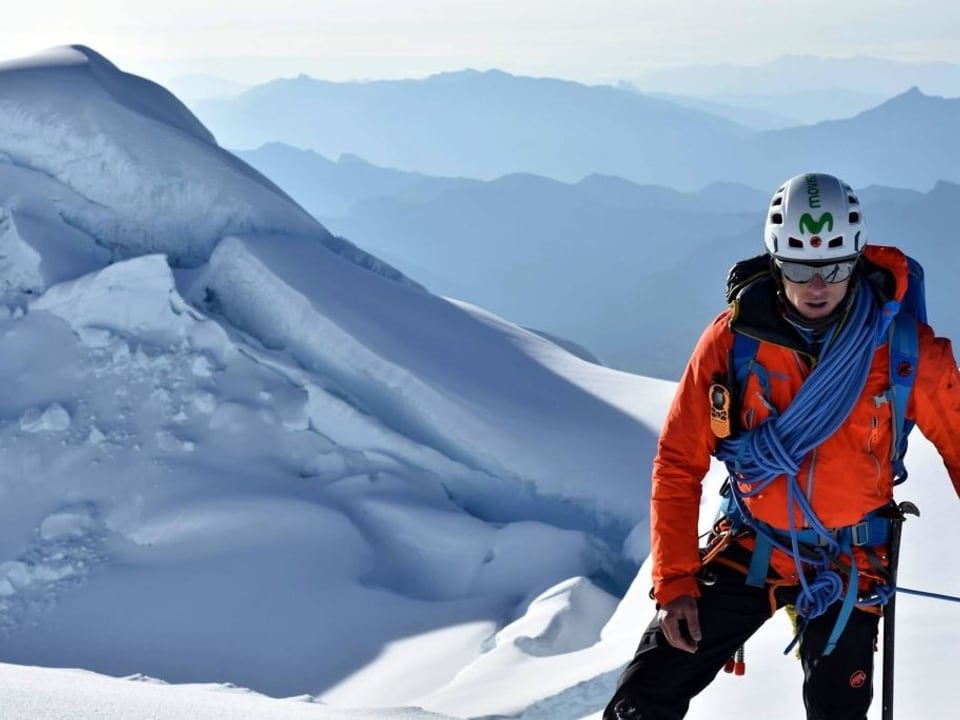 Bergsteiger auf verschneitem Gipfel mit Kletterausrüstung.