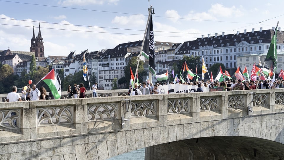 Auf der Mittleren Brücke in Basel marschieren Demonstrierende mit rot-grün-weiss-schwarzen Palästina-Fahnen.