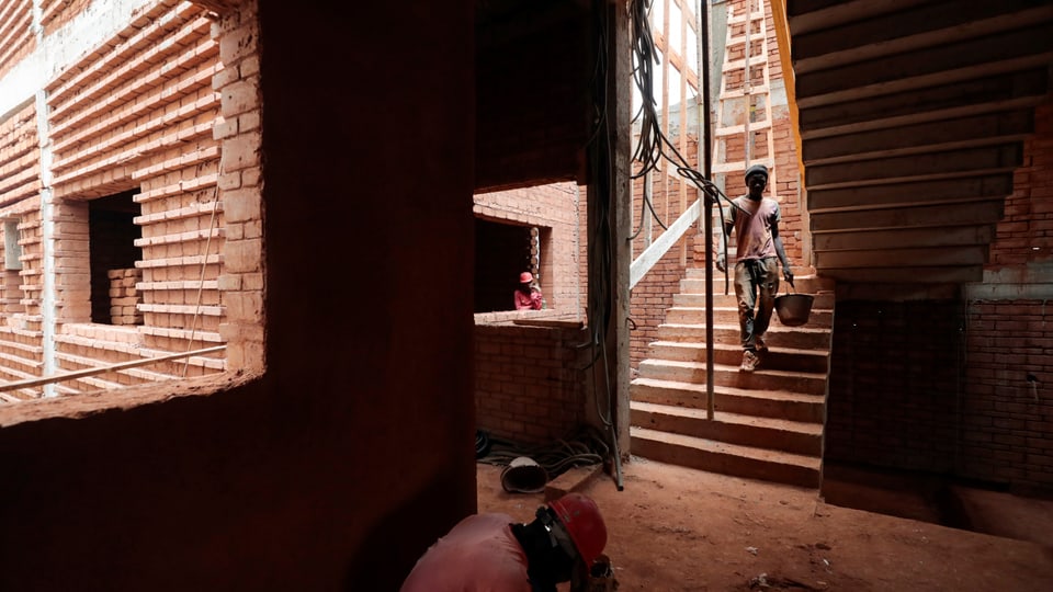 Arbeiter gehen und tragen Baumaterial in einem Backsteingebäude im Bau.