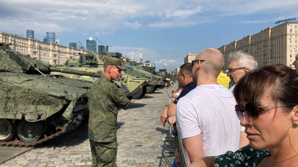 Several tanks are lined up and a soldier appears to be explaining.