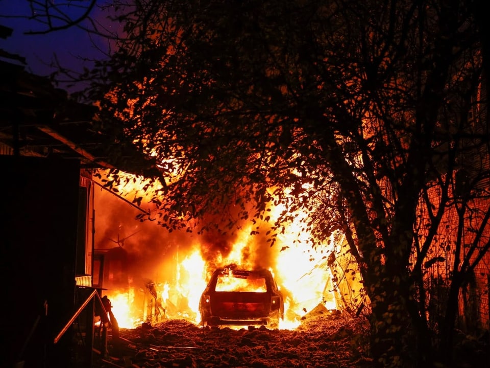 Auto in Flammen neben einem Gebäude bei Nacht.