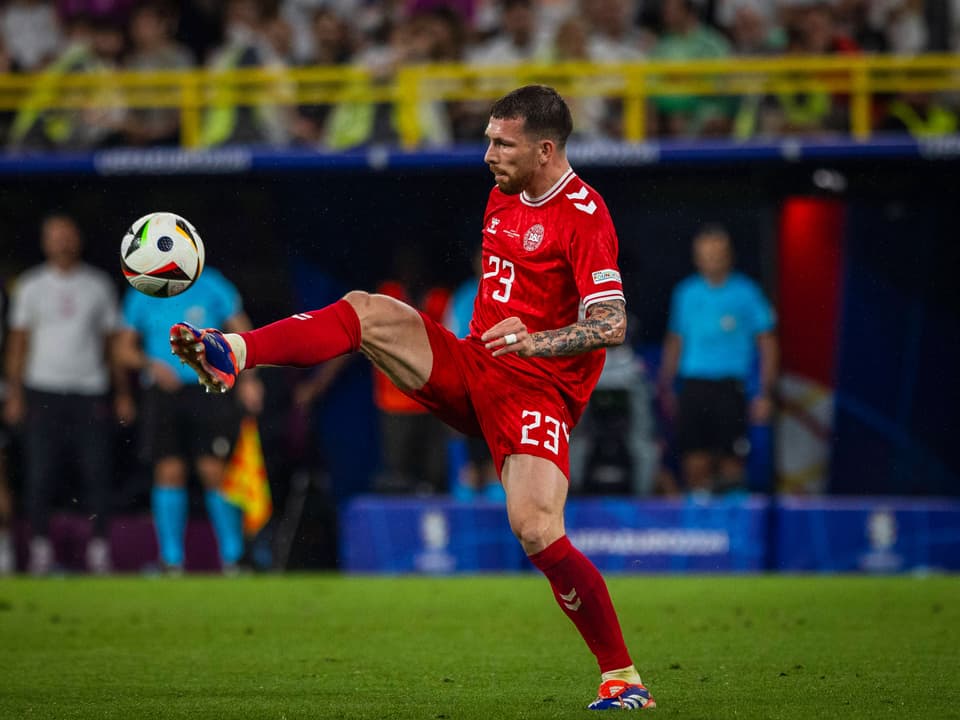 Fussballspieler in rotem Trikot kontrolliert Ball im Spiel.