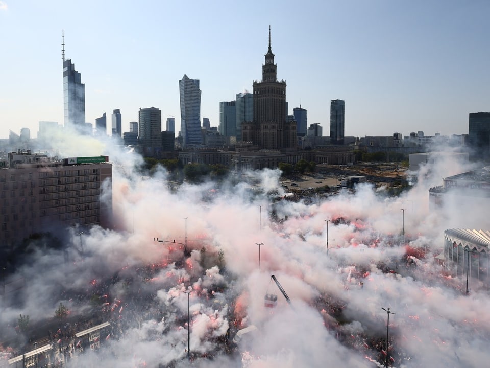 Menschenmenge mit Rauchfackeln in einer Stadt mit Wolkenkratzern im Hintergrund.