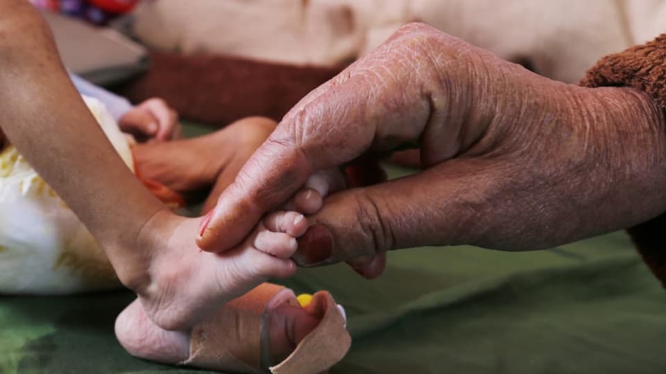 Eine alte Hand hält einen Baby-Fuss
