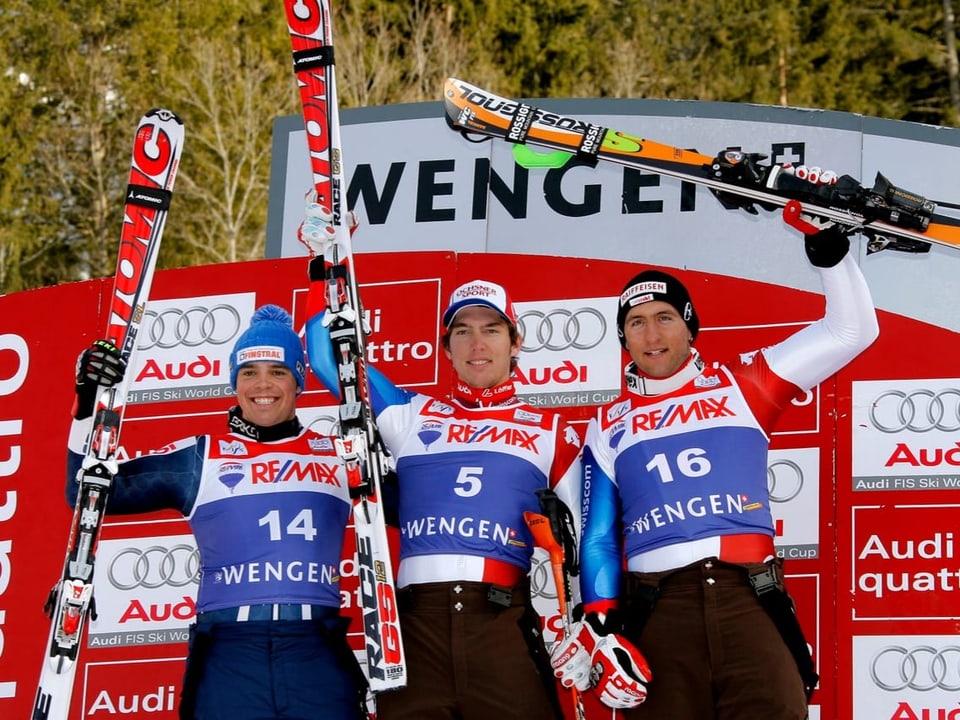 Drei Männer auf dem Podest mit Ski in der Hand, Janka in der Mitte.