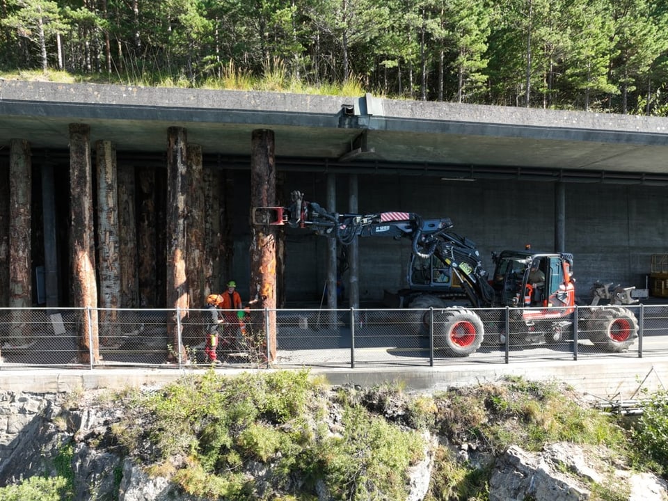 Forstarbeiter mit schwerem Gerät vor einer Betonwand im Wald.