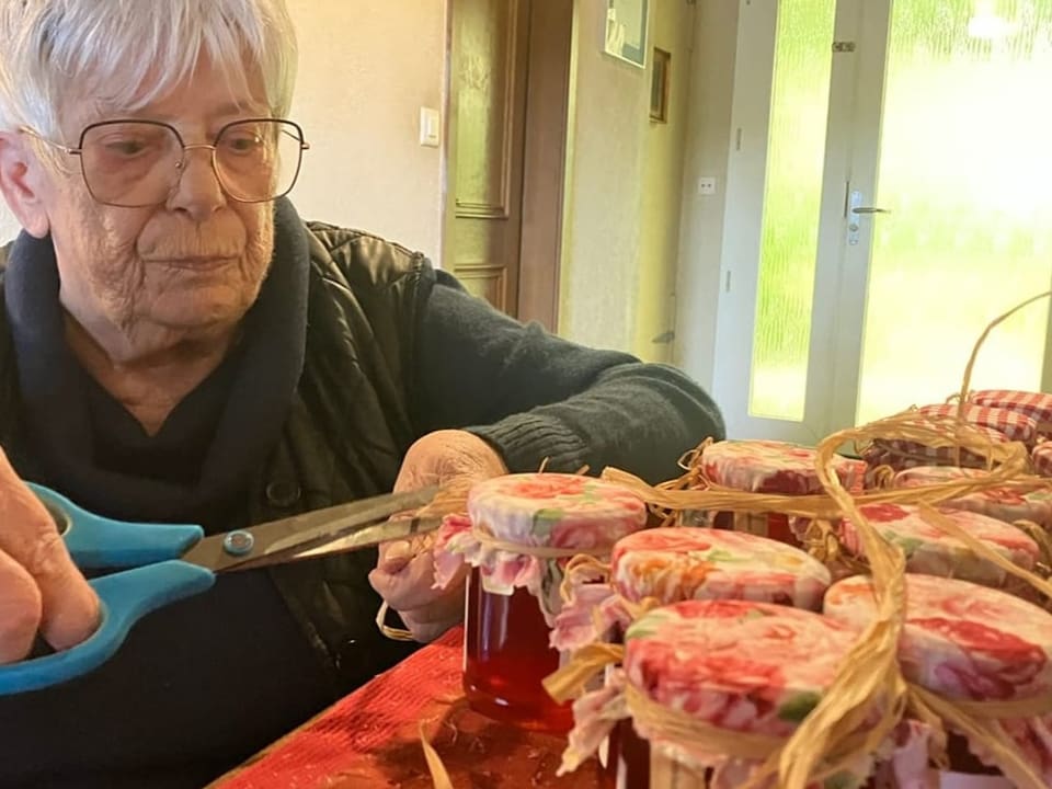 Frau mit Schere an Tisch mit dekorativen Marmeladengläsern.