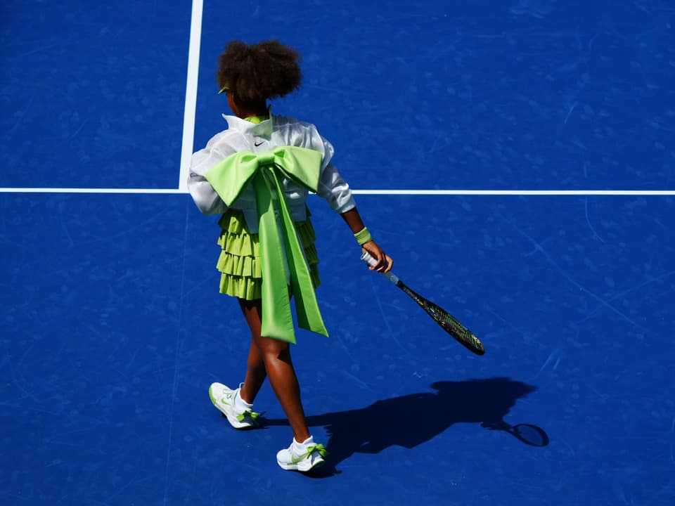 Tennisspielerin in grünem Outfit auf blauem Platz.