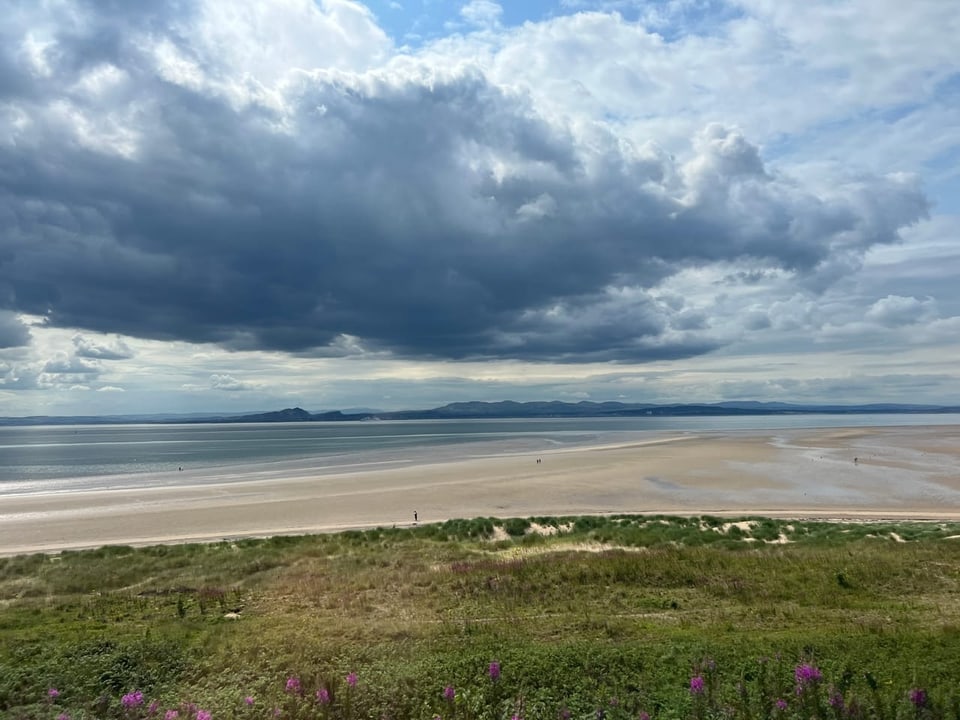 Weitläufiger Strand mit Wolken am Himmel.