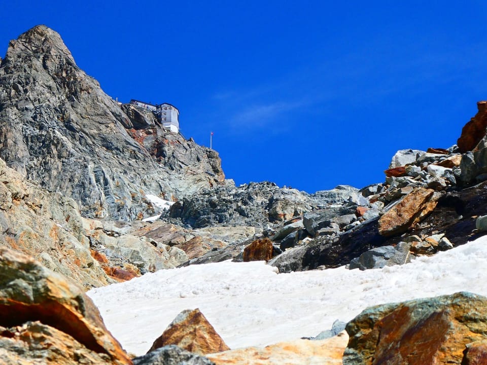Felsen und Schnee unter blauem Himmel mit Berghütte.