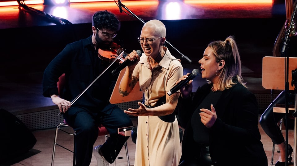 Stefanie Heinzmann stehend singend zwischen einer Backgroundsängerin und einem Violisten