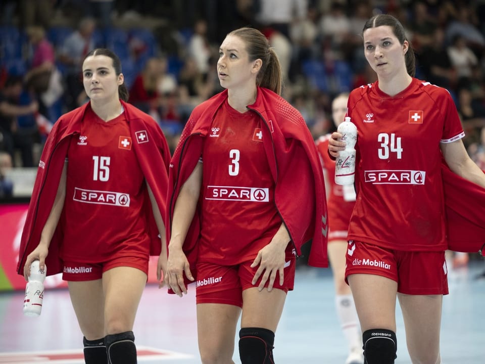 Drei Handballspielerinnen im roten Trikot auf dem Spielfeld.