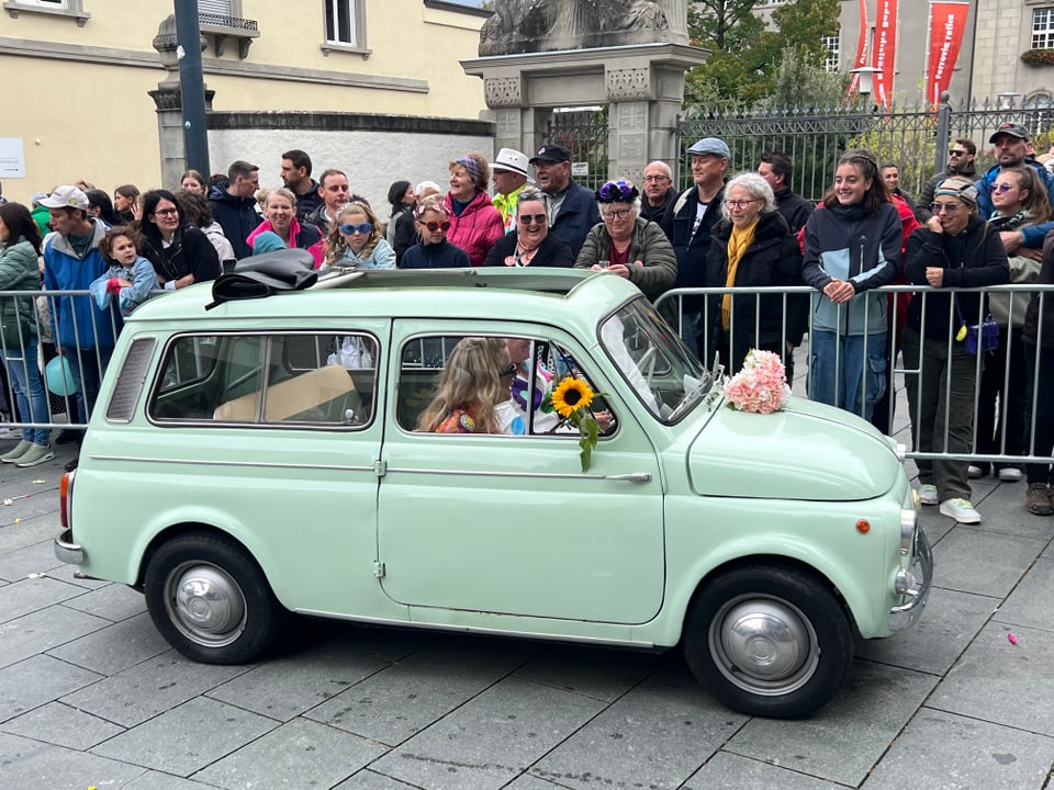 Grüne Retro-Auto-Parade mit Zuschauern hinter Absperrungen.