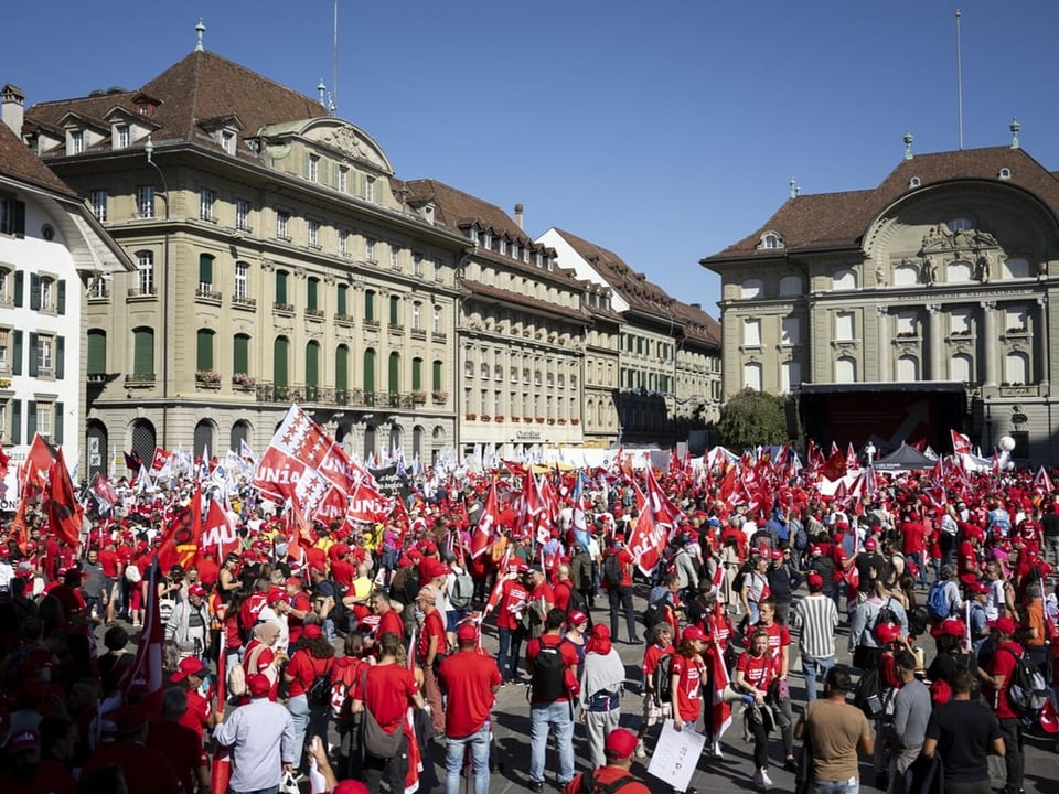 Menschenmenge in roten Kleidern vor alten Gebäuden in einer Stadt.