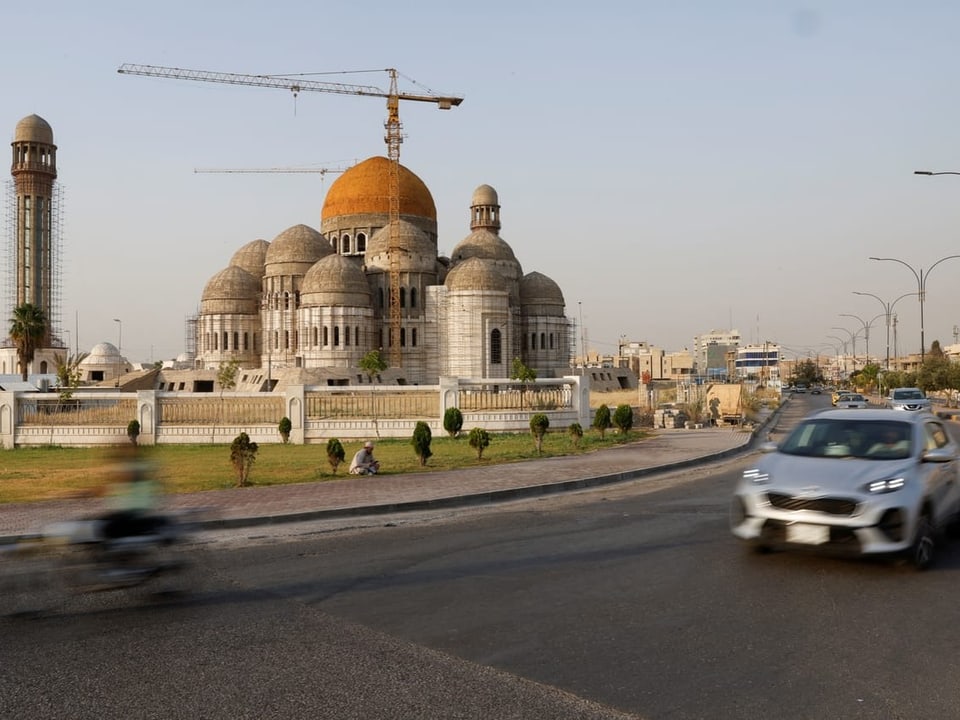 Grosse Moschee mit orangefarbener Kuppel und vorbeifahrenden Fahrzeugen.