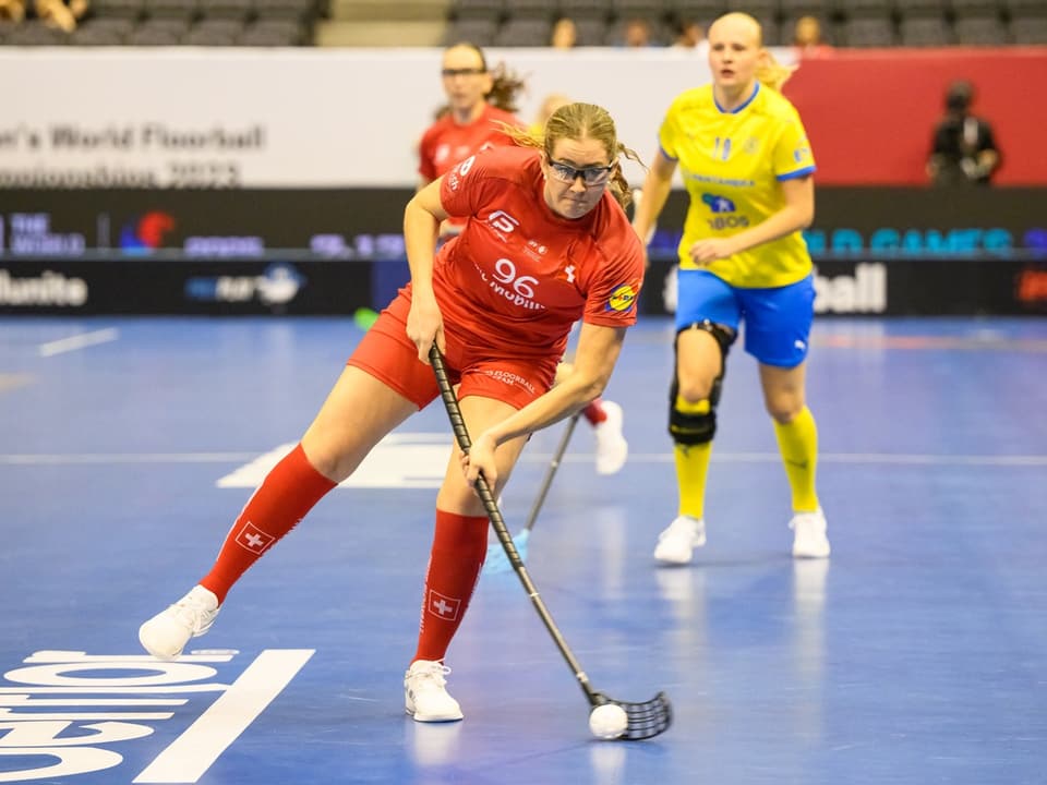 Floorball-Spielerin in rotem Trikot am Ball während eines Spiels.