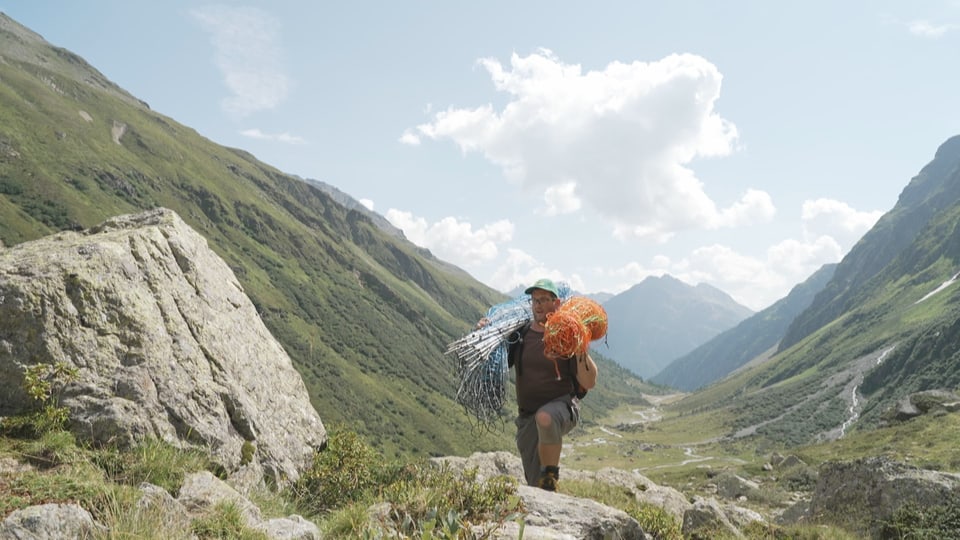 Person trägt Netze in alpiner Berglandschaft.