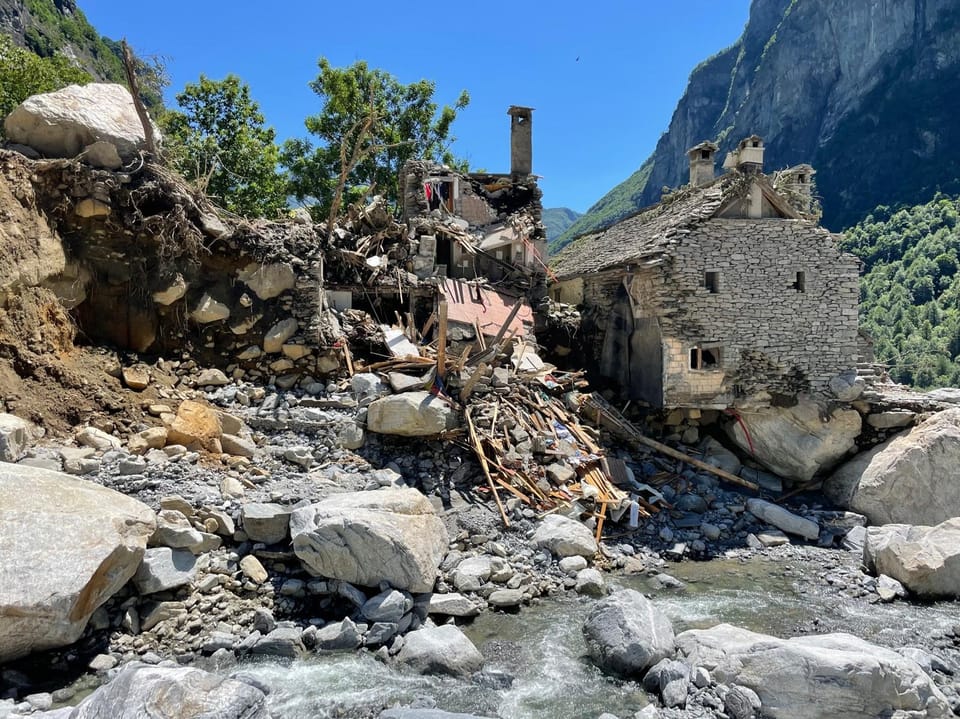 Zerstörte Häuser nach einem Erdrutsch in bergiger Landschaft.