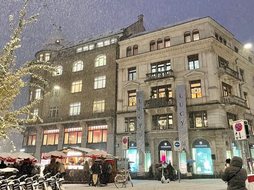 Verschneite Strassenszene mit beleuchteten Gebäuden und Marktständen.