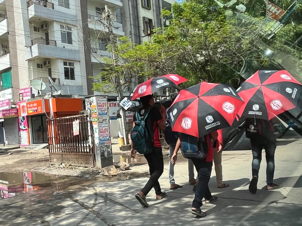 Studierende mit schattenspendenden Regenschirmen.